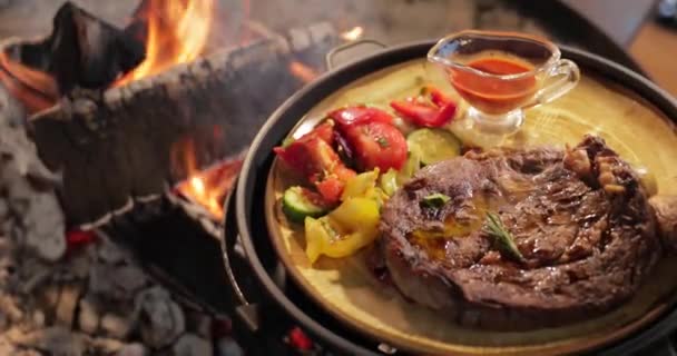 구운 고기와 야채의 가장 큰 부분은 접시 위에 놓여 있습니다. 쥬시 쇠고기 스테이크, 맨 뒤에 있는 커다란 불꽃, 소스, 붉은 석탄, 연기, 장작, 초경량, 느린 움직임 — 비디오