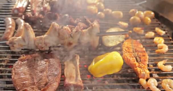 A carne conserva-se em escabeche em uma treliça da grelha, umas costelas, uma estaca, umas Enchidos, umas bordas, um frango, chama nua, um pimentão doce amarelo, garras de metal, o cozinheiro vira a carne, uma fumaça, lenha, vapor, de perto — Vídeo de Stock