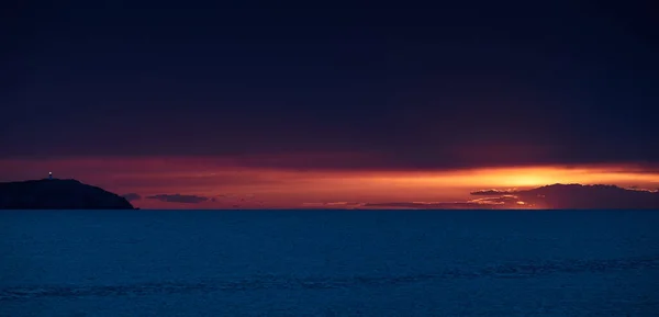 A világítótorony a hegyen naplementekor, a narancssárga ég, a csendes tenger, a napsütés útja. — Stock Fotó