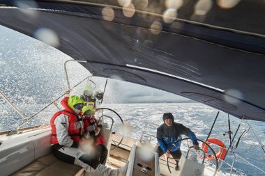 İspanya, Malorca, 29 Nisan 2018: Fırtına sırasında yatta çocuklu bir aile, direksiyon başında, yüzlerine su geçirmez giysiler ve güneş gözlüğü takıyor.