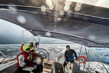 İspanya, Malorca, 29 Nisan 2018: Fırtına sırasında yatta çocuklu bir aile, direksiyon başında, yüzlerine su geçirmez giysiler ve güneş gözlüğü takıyor.