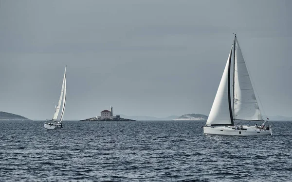 Segelboote wetteifern bei Sonnenuntergang um eine Segelregatta, Segelregatta, Reflexion der Segel auf dem Wasser, mehrfarbiger Spinaker, Bootsnummer achtern Boote, große weiße Wolken, die Insel mit einem Leuchtturm — Stockfoto