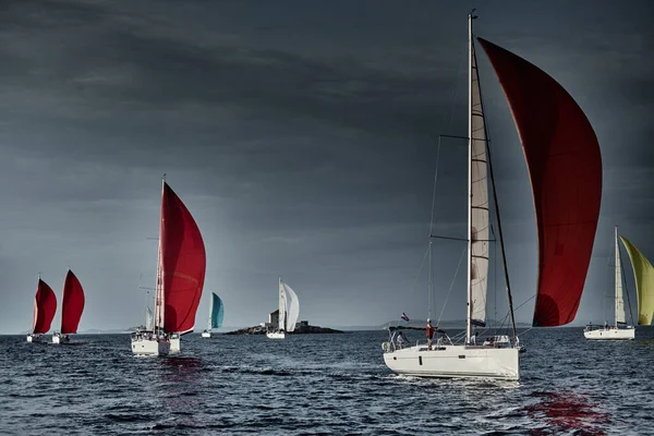 Segelboote wetteifern bei Sonnenuntergang um eine Segelregatta, Segelregatta, Reflexion der Segel auf dem Wasser, mehrfarbiger Spinaker, Bootsnummer achtern Boote, große weiße Wolken, die Insel mit einem Leuchtturm — Stockfoto