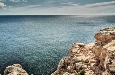 Balistik denizin manzarası ve olanaksız dağlar, gök mavisi su, fırtına gökyüzü, dağların tepesindeki yalnız binalar, arka planda yelkenli teknesi.