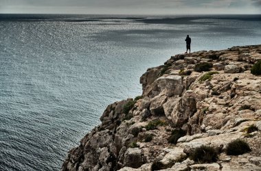 Balistik denizin manzarası ve olanaksız dağlar, gök mavisi su, fırtına gökyüzü, kayanın kenarındaki yalnız insan, güneşli hava.