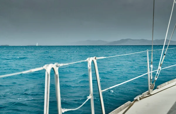 La vue sur la mer et les montagnes depuis le voilier, bord d'une planche du bateau, élingues et cordes, éclaboussures sous le bateau, temps pluvieux, ciel dramatique — Photo