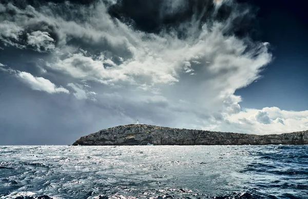 Faro está en el borde de la roca, el paisaje del mar baleárico y montañas improbables, agua azul, el cielo de tormenta, montañas — Foto de Stock