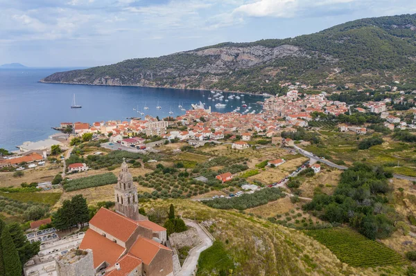 Vista panorámica aérea de la catedral de San Nicolás en la ciudad de Komiza - la de numerosas ciudades portuarias en Croacia, techos naranjas de casas, pintoresca bahía, montaña está en el fondo — Foto de Stock