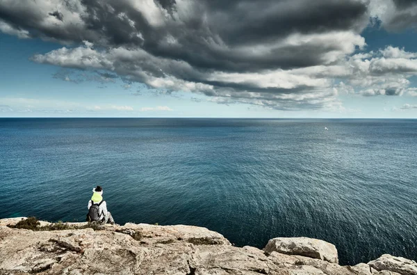 The Landscape of the balearic sea and improbable mountains, azure water, the storm sky, lonely person on the edge of the rock, sunny weather Stock Picture