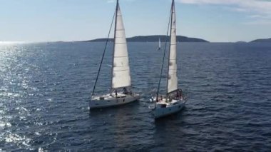 Hırvatistan, Adriyatik Denizi, 18 Eylül 2019: Birbirine yakın iki yelkenli yatı, gençlerin yatlarda eğlenmesi, gençlerin kayıklar arasında bir halata tutunması, arka planda adalar, suda güneş yansıması