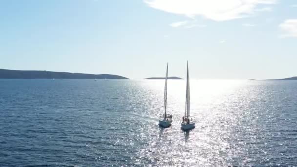 Dois iates de vela estreitamente um a outro, os jovens divertem-se em iates, os jovens suspendem-se em uma corda entre barcos, o Mar Adriático, a Croácia, ilhas em um contexto, reflexões de sol na água, calma — Vídeo de Stock