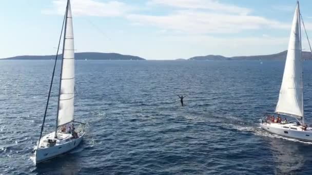 Два вітрильних яхти близько один до одного, молодь розважається на яхтах, молоді люди висять на мотузці між човнами, Адріатичне море, Хорватія, острови на задньому плані, сонячні роздуми на воді, спокій. — стокове відео