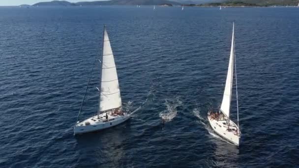 Две парусные яхты близко друг к другу, молодежь веселится на яхтах, молодежь висит на веревке между лодками, Адриатическое море, Хорватия, острова на заднем плане, солнечные размышления на воде, спокойствие — стоковое видео