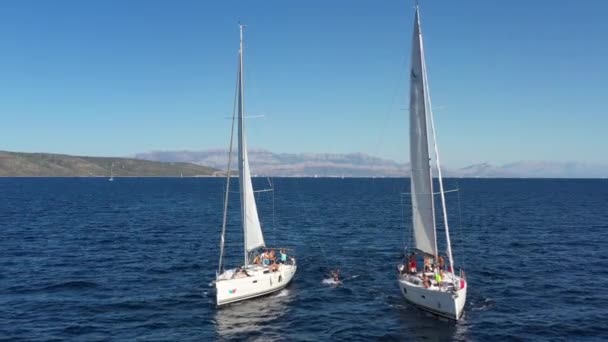 Croácia, Mar Adriático, 18 Setembro 2019: Dois iates à vela de perto um do outro, os jovens se divertem em iates, os jovens penduram em uma corda entre barcos, ilhas em um fundo, reflexão do sol sobre a água — Vídeo de Stock