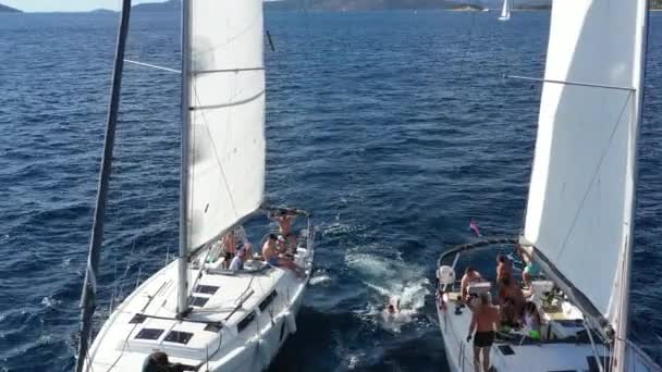 Croatia, Adriatic Sea,18 September 2019: Two sailing yachts closely to each other, youth have fun on yachts, young people hang on a rope between boats, islands on a background, sun reflection on water — Stock Video