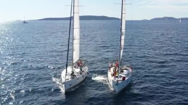 Croacia, Mar Adriático, 18 de septiembre de 2019: Dos yates de vela muy cerca entre sí, los jóvenes se divierten en yates, los jóvenes cuelgan de una cuerda entre barcos, las islas en un fondo, reflejo del sol en el agua — Vídeos de Stock