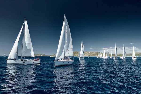 Segelboote konkurrieren bei Sonnenuntergang bei einer Segelregatta, Regatta der Segelboote, Reflexion der Segel auf dem Wasser, bunte Spinnaker, Anzahl der Boote auf Achterbooten, Helle Farben — Stockfoto