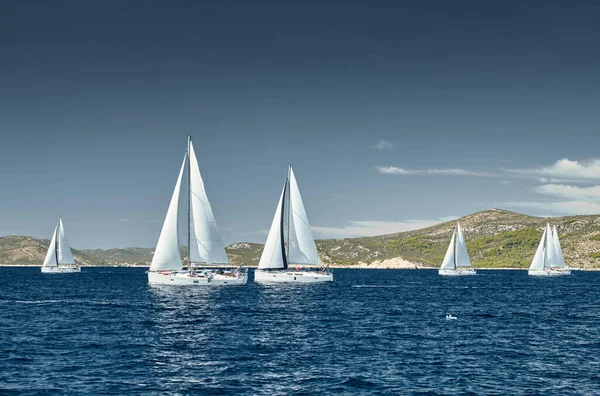 Segelboote messen sich bei einer Segelregatta bei Sonnenuntergang, Regatta der Segelboote, Reflexion der Segel auf dem Wasser, bunte Spinnaker, Anzahl der Boote auf Achterbooten, Insel im Hintergrund, klares Wetter — Stockfoto