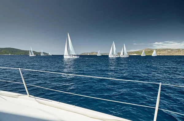 Veleiros competem em uma regata de vela ao pôr do sol, corrida de veleiros, reflexão de velas na água, spinnakers multicoloridos, número de barco está em barcos de popa, ilha está em segundo plano, tempo claro — Fotografia de Stock