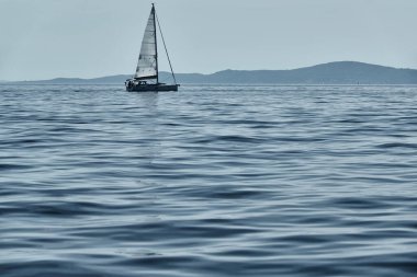 Güzel deniz manzarası, ufukta yalnız bir tekne, arka planda parlak renkler var.