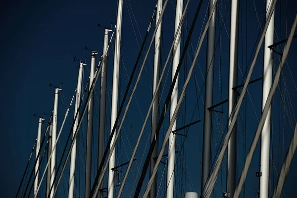 The number of masts of sailboats with the blue sky on a background, a sail regatta, reflection of masts on water, ropes and aluminum, Bright colors — Stock Photo, Image