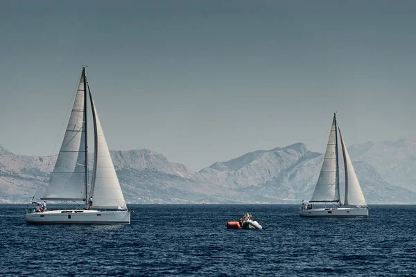 Das Gummiboot der Organisatoren einer Regatta mit dem Richter und Ballon von oranger Farbe, Das Rennen der Segelboote, Intensiver Wettbewerb, Insel mit Windmühlen im Hintergrund — Stockfoto