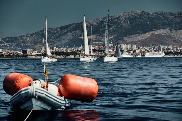 El bote de goma de los organizadores de una regata con el juez y globo de color naranja, La carrera de veleros, Competencia intensa, isla con molinos de viento están en el fondo — Foto de Stock