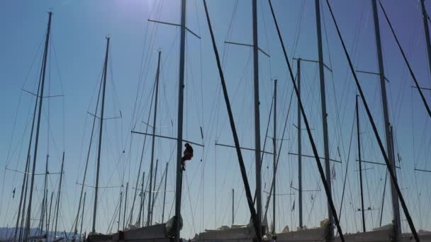 Croatia, marina Kastela, 15 September 2019: Drone view point of the sailor hangs in a cradle on a mast and binds flags, participant of a sailing regatta, people is waiting for the forthcoming race — Stock Video