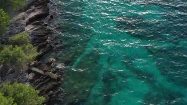 Foto aérea de la costa rocosa del mar con agua de color azul al atardecer, árboles verdes, reflejo del sol sobre el agua — Vídeos de Stock