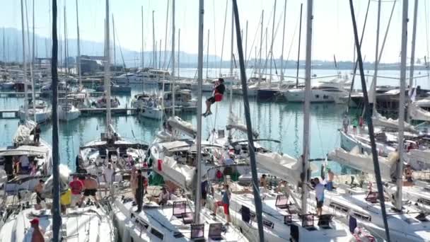 Croatia, marina Kastela, 15 September 2019: Drone view point of the sailor hangs in a cradle on a mast and binds flags, participant of a sailing regatta, people is waiting for the forthcoming race — Stock Video
