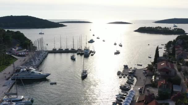 Luftaufnahme der Marina Maslinica auf der Insel Solta bei Sonnenuntergang, Kroatien, viele Segelboote, orangefarbene Dächer, Sonnenreflexe auf dem Wasser, grüne Bäume — Stockvideo