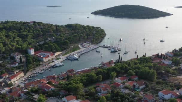 Letecký pohled na přístav Maslinica na ostrově Šolta při západu slunce, Chorvatsko, mnoho plachetnic, střechy oranžové barvy, sluneční odrazy na vodě, zelené stromy — Stock video