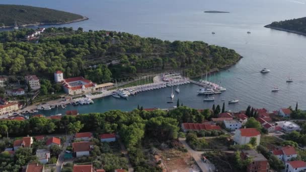Letecký pohled na přístav Maslinica na ostrově Šolta při západu slunce, Chorvatsko, mnoho plachetnic, střechy oranžové barvy, sluneční odrazy na vodě, zelené stromy — Stock video