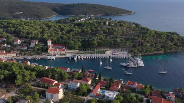 Luftaufnahme der Marina Maslinica auf der Insel Solta bei Sonnenuntergang, Kroatien, viele Segelboote, orangefarbene Dächer, Sonnenreflexe auf dem Wasser, grüne Bäume — Stockvideo