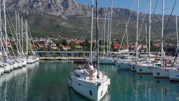 Kroatië, jachthaven Kastela, 15 september 2019: Deelnemer aan een zeilregatta met boten op een achtergrond, de boot verlaat de haven, mensen wachten op de komende race, skiërs en zeilers — Stockvideo