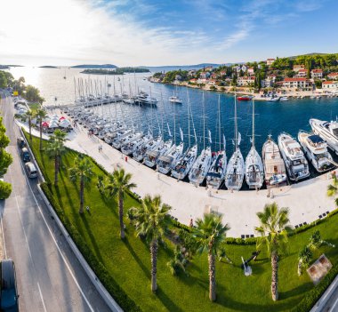 Hırvatistan, Maslinica, 15 Eylül 2019: Günbatımında eşit hizada yelkenli yelkenlilere demirli insansız hava aracı bakış açısı, yelkenli yarışlarına katılan insanlar yarış günü, gök mavisi suyu ve rıhtımdan sonra dinleniyor