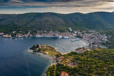 Aerial view of marina Vis at sunset, Croatia, a lot of chaotically standing boats in a bay, roofs of orange color, sunshine, hills with green trees, ferry station clipart