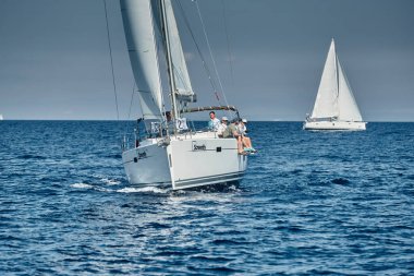 Hırvatistan, Adriyatik Denizi, 17 Eylül 2019: Yelkenli yarışı, ekip bir kayık tahtasının kenarında, bir yelkenli yarışı, yoğun rekabet, parlak renkler ve deniz fenerli ada arka planda bulunuyor, 