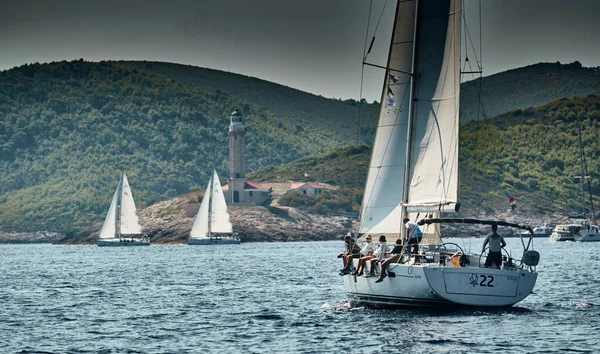 Kroatien, Adria, 17. September 2019: Das Rennen der Segelboote, das Team sitzt am Rand eines Bootsbretts, eine Regatta, Intensiver Wettbewerb, leuchtende Farben, Insel mit Leuchtturm im Hintergrund, — Stockfoto