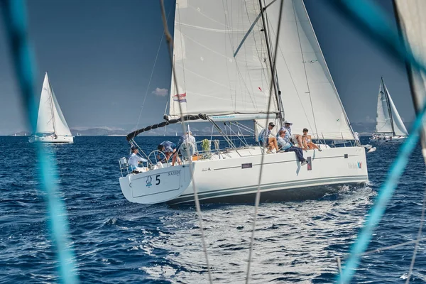 Croatia, Adriatic Sea, 17 September 2019: The race of sailboats, the team sits on the edge of a boat board, a regatta, Intense competition, bright colors, island with lighthouse are on background, — Stock Photo, Image