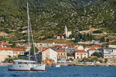 Hırvatistan 'ın sayısız liman kasabasından biri olan Komiza şehrinin deniz manzarası, ön planda Katamaran, evlerin turuncu çatıları, St. Nicholas katedrali, dağların Picturesque yamaçları.
