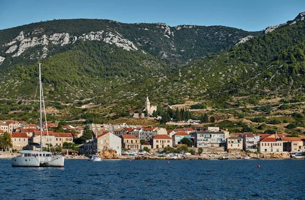 El paisaje marino de la ciudad Komiza - una de las ciudades portuarias numerosas en Croacia, el Catamarán en primer plano, los techos anaranjados de las casas, la catedral San Nicolás, las laderas pintorescas de las montañas — Foto de Stock