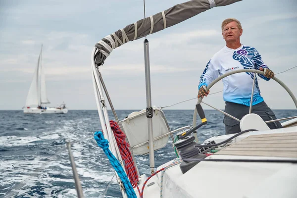 Croacia, Mar Adriático, 19 Septiembre 2019: El capitán brutal del barco está en un volante, chaqueta de color azul, velero competir en una regata de vela, tiempo nublado — Foto de Stock