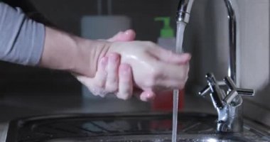 Adam su altında ellerini dezenfektanla yıkıyor şişe jeline bastırıyor arka planda kağıt havlu rulosu, koronavirüs salgını sırasında el derisini dezenfekte ediyor COVID-19 salgını, virüs yayılıyor.