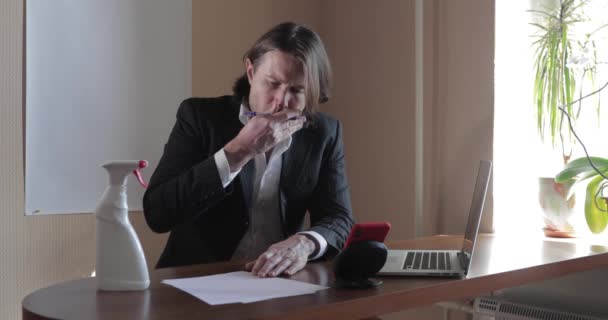 Der schöne Geschäftsmann im Anzug bleibt zu Hause, er hustet stark, er arbeitet am Laptop auf dem Tisch, Flasche Antiseptikum, hält eine Konferenz ab, ferne Arbeit während einer Pandemie Covid-19, Quarantäne — Stockvideo