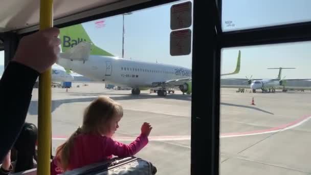 Riga, 23 april 2019: Het kleine meisje zit in de bus bij een raam, Levering aan het vliegtuig, de bus gaat van het vliegveld terminal naar het vliegtuig, veel vliegtuigen zijn in het veld bij een zonnig weer — Stockvideo