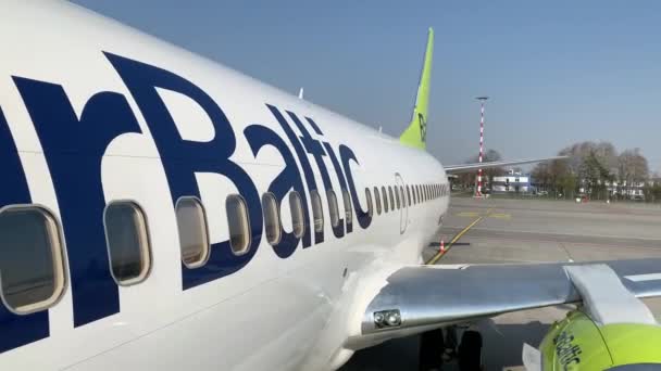 Letónia, Riga, 23 de abril de 2019: Janelas de avião, sem pessoas, tempo de primavera ensolarado, céu azul, logotipo da Air Baltic, turbina, asa de avião — Vídeo de Stock