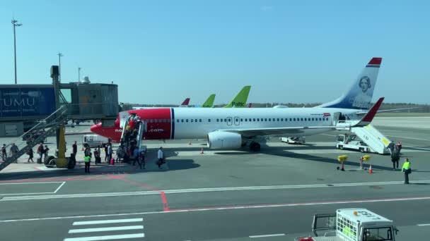 Letonya, Riga, 23 Nisan 2019: Uçaklara giden bir merdivene binen yolcular, Norveç havayolları uçağına binen yolcular, güneşli bahar havası, el bagajı, merdiven basamakları, mavi gökyüzü — Stok video