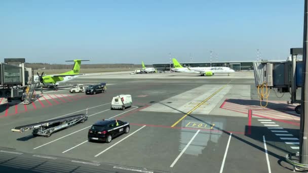 Lotyšsko, Riga, 23. dubna 2019: Pohled z okna letadel na provoz a přípravu k letu na poli letiště, Čerpací stanice, úklid letadel, slunečné jarní počasí — Stock video
