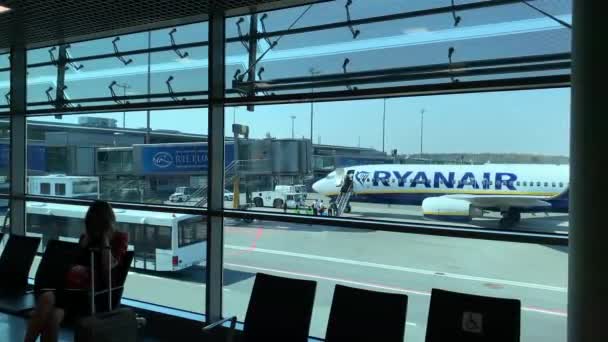 Latvia, Riga, 23 April 2019: Passengers sit on benches waiting for boarding to plane, windows overlooking a airport field with plane of Ryanair airlines, a glossy floor — Stock Video
